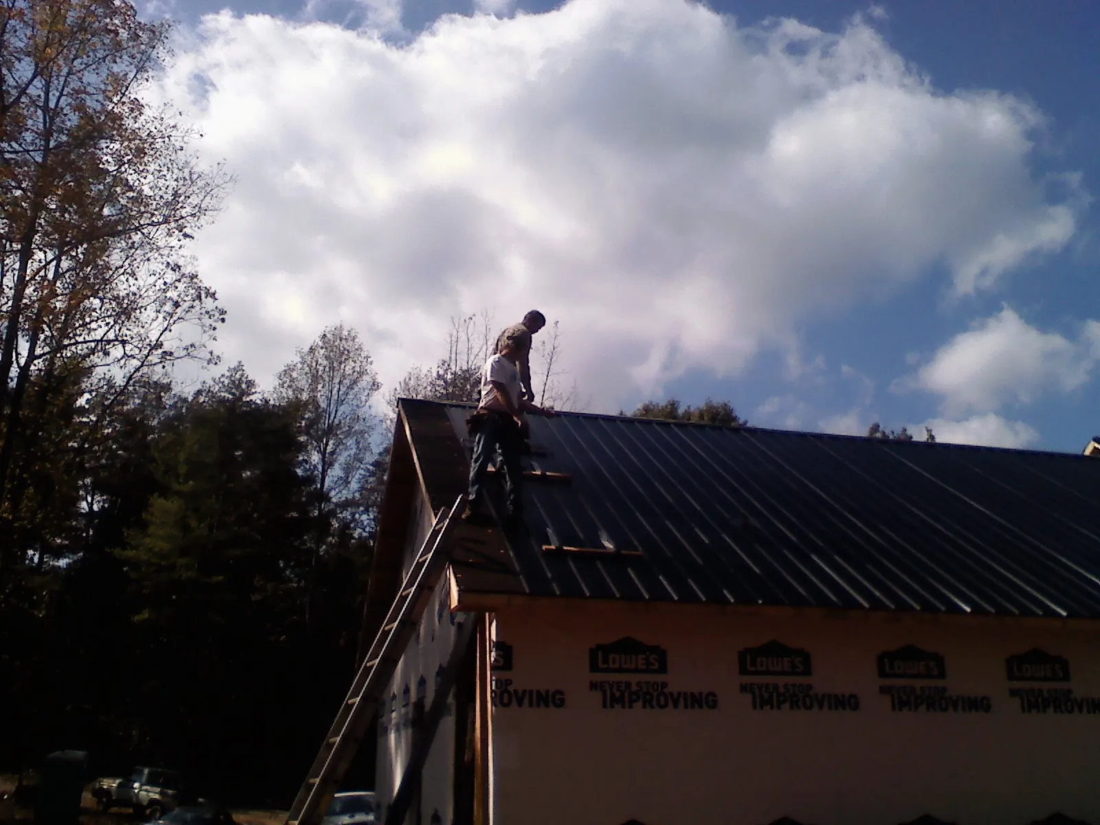 Roofer fastening dark metal panels high against a cloudy sky, from a Roof Inspection job in Paulden